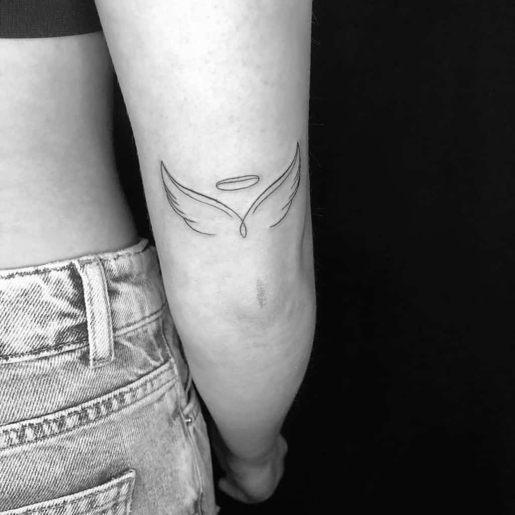 Minimalist line tattoo of an angel wings with a halo above it