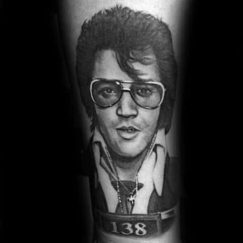 Black and grey Elvis Presley tattoo styled like a mugshot, featuring his iconic glasses, open collar, and number 138 plaque.