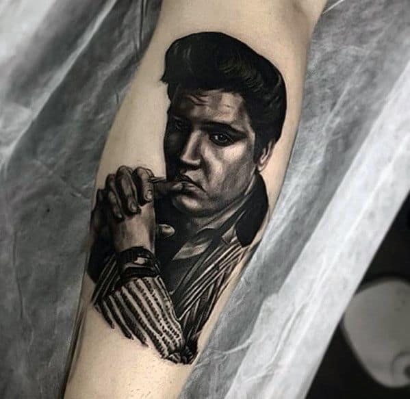 Detailed black and grey Elvis Presley tattoo on forearm, showing him in a reflective pose with hands clasped and intense gaze.