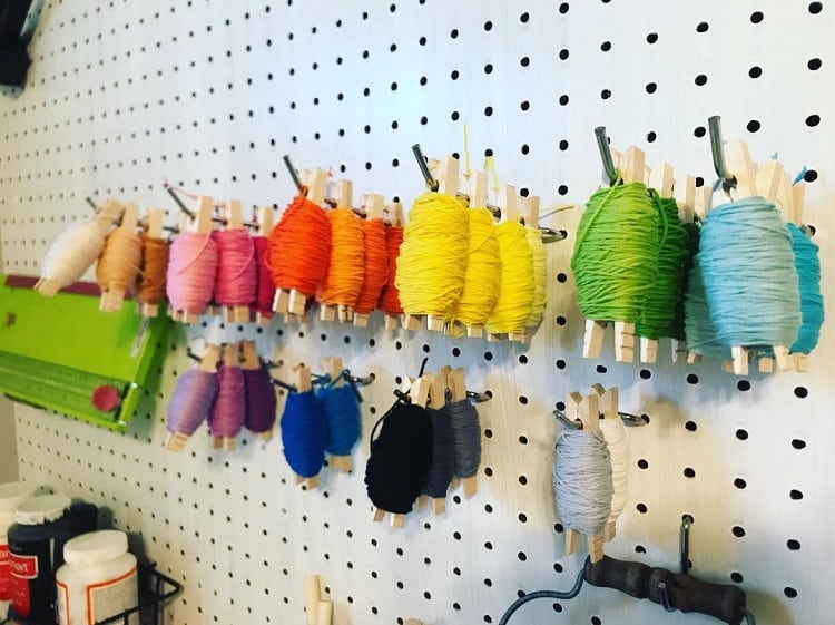 Colorful yarn spools hanging on a pegboard, organized by hue