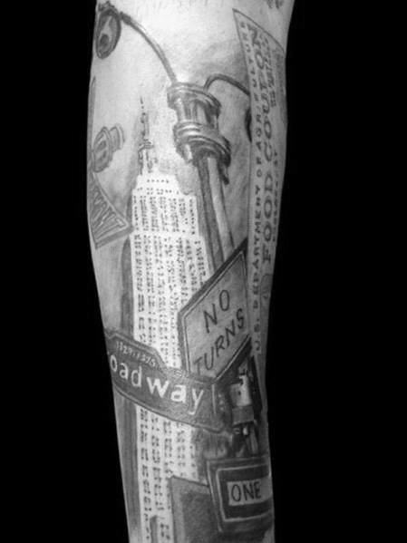 Empire State Building tattoo surrounded by street signs, lamp posts, and NYC elements, inked realistically on a man's forearm.