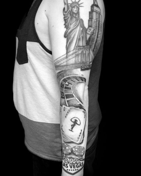 Full-arm tattoo combining Empire State Building, Statue of Liberty, Brooklyn Bridge, and Las Vegas symbols in bold black ink.