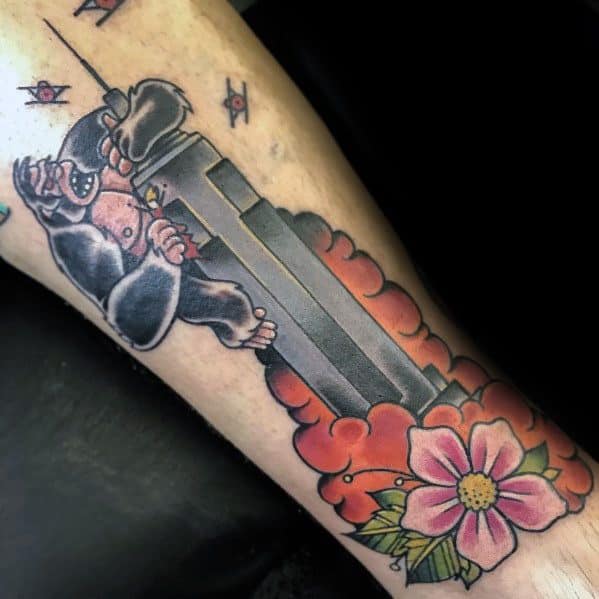 Vibrant tattoo of King Kong climbing the Empire State Building, accented by colorful floral elements on a man's forearm.