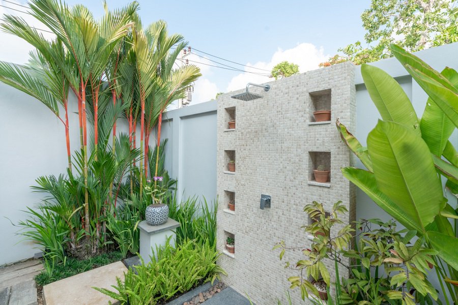 Outdoor shower with tiled wall, built-in planters, and vibrant tropical plants in a private garden