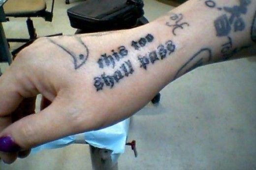 "This Too Shall Pass" tattoo on the inner forearm, with other tattoos visible around it.