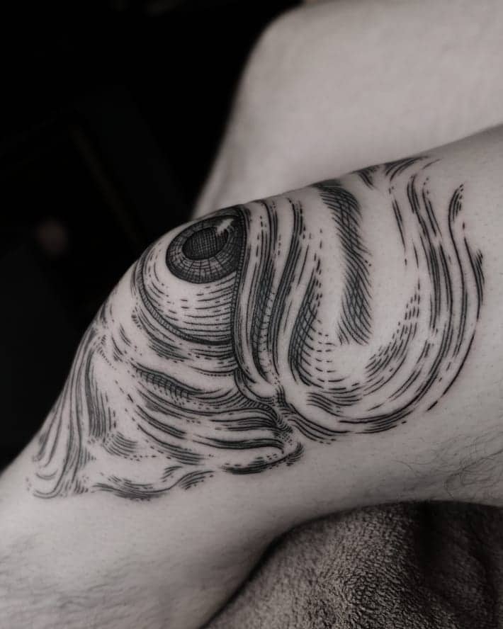 Tattoo of a surreal all-seeing eye integrated into flowing, abstract skin-like patterns, inked in black on the inner elbow.