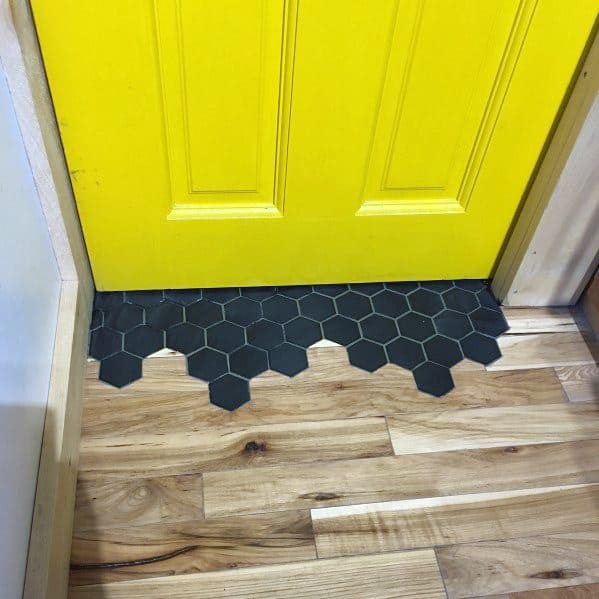 Bold tile-to-wood floor transition at a yellow door, featuring black hexagonal tiles blending into natural wood planks seamlessly