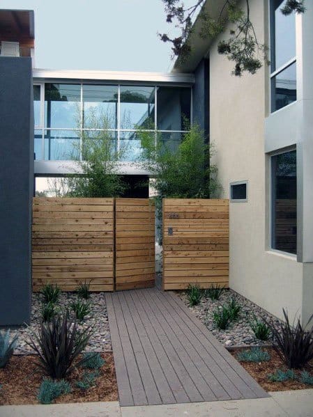 Modern house with a wooden fence gate, gravel path, and plants in front