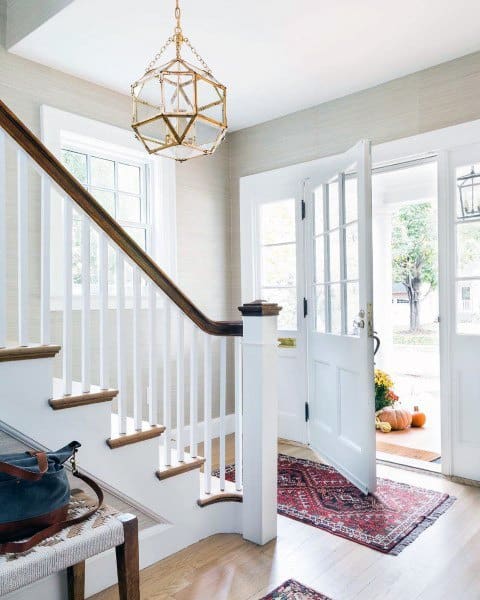 Bright entryway with open door, rug, staircase, and pumpkins outside; geometric chandelier and natural light fill the space