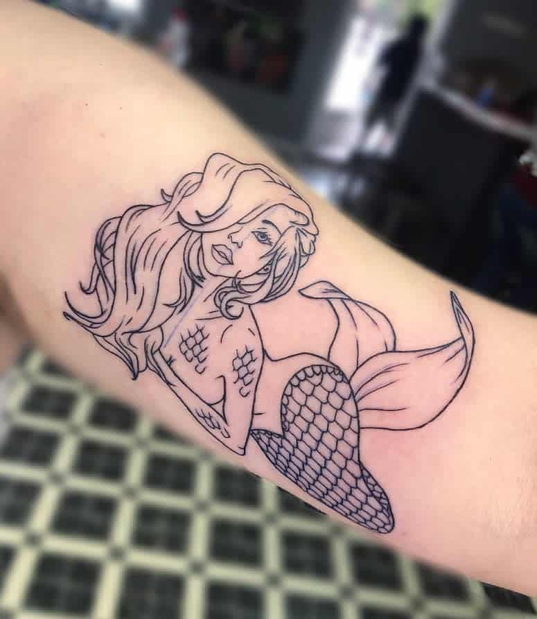 Minimalist black line tattoo of a mermaid with flowing hair, expressive eyes, and delicate scale details on her tail.