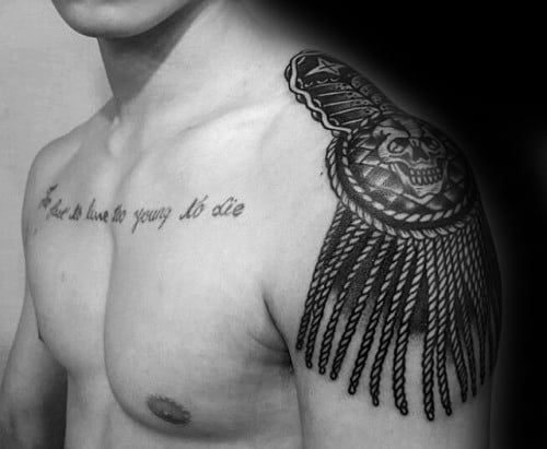 Epaulette tattoo with a fierce skull emblem, braided details, and long rope tassels draping over the upper arm.