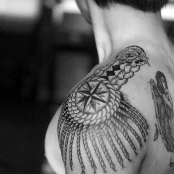 Compass-themed epaulette tattoo with braided detailing and flowing tassels, placed on the upper shoulder and back.