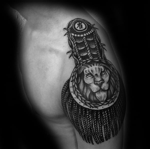 Majestic epaulette tattoo with a fierce lion portrait, braided border, detailed textures, and long tassels draping the upper arm.