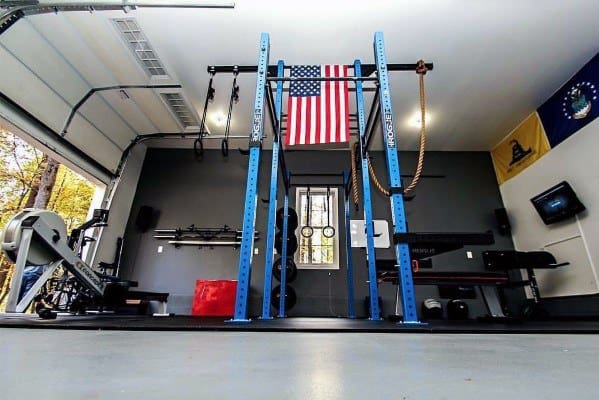 Garage gym with blue power rack, rope, American flag, and wall-mounted equipment storage.