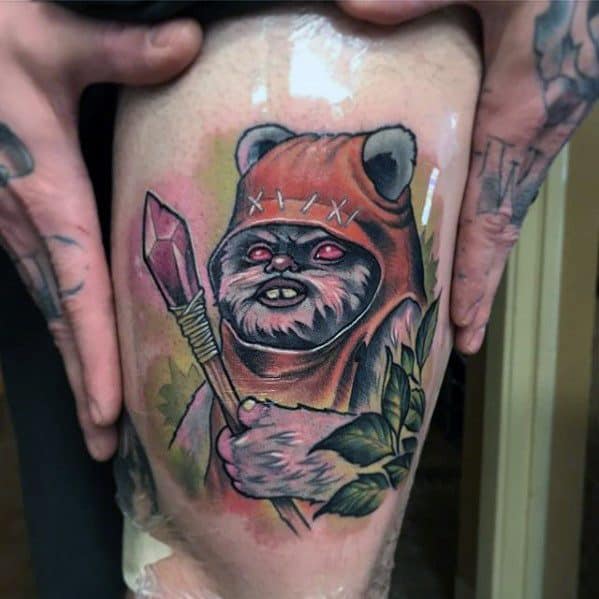 Brightly colored Ewok tattoo with glowing red eyes, holding a spear and accented by green leaves and a pink background glow.