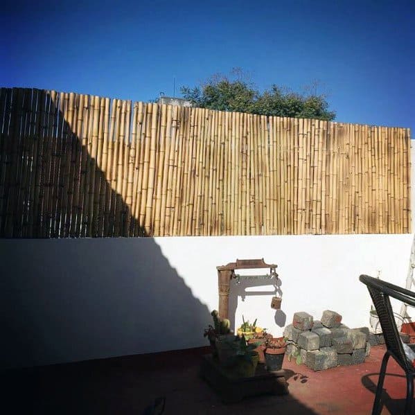 Bamboo privacy fence on top of a white concrete wall in a sunny patio with garden decor.