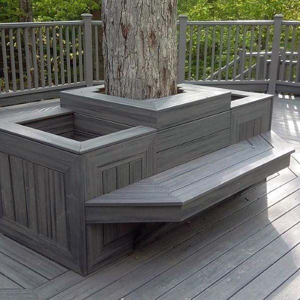 A wooden deck with a built-in bench wraps around a tree, boasting stylish planters and railing