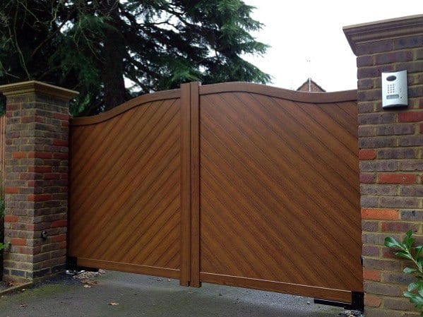 Wooden gate with a chevron pattern between brick pillars, surrounded by trees and featuring an intercom system