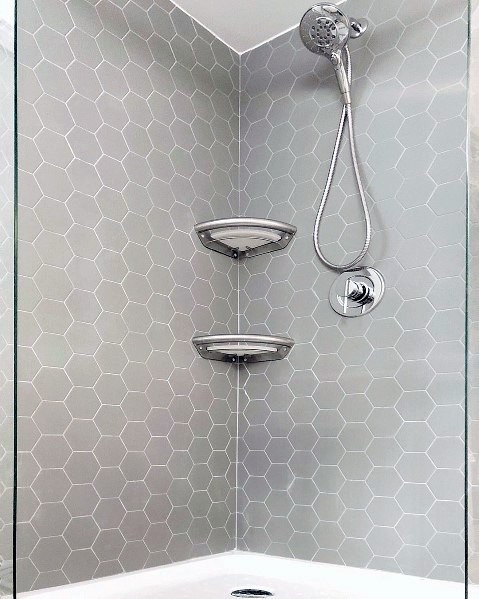 Corner shower area with hexagonal gray tiles, a detachable showerhead, and two shelves