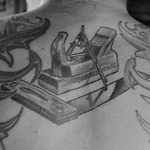 Black and gray back tattoo featuring a wood plane, compass, and ruler, symbolizing precision, craftsmanship, and dedication to woodworking.