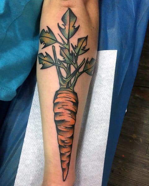 Bold and colorful carrot tattoo on the forearm, featuring vibrant orange shading, dark outlines, and detailed green leaves for a striking design.