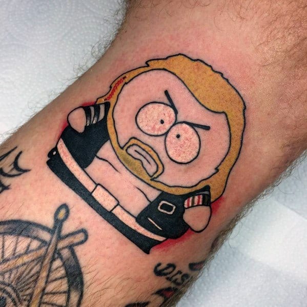 South Park-style tattoo featuring a bearded character with long blonde hair, wearing a black vest and white shirt, done in bold colors.