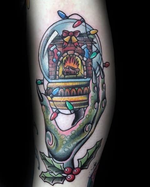 Christmas tattoo of a green Grinch-like hand holding a festive snow globe with a cozy fireplace inside, wrapped in colorful holiday lights and holly.