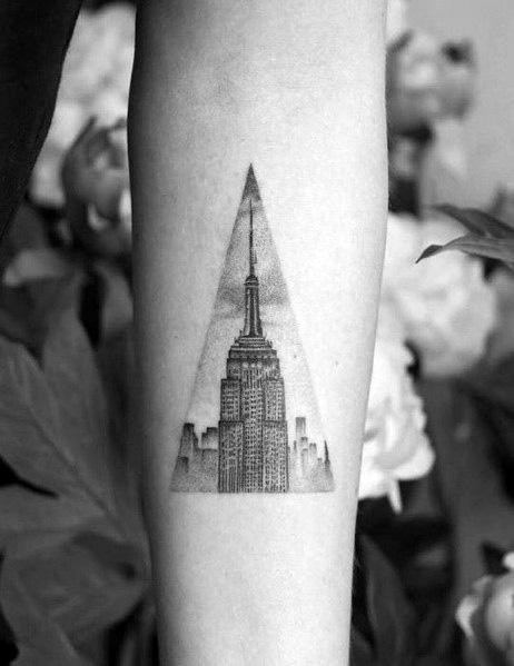Empire State Building skyline tattoo neatly enclosed in a triangular frame, shaded in black ink on a man's inner forearm.
