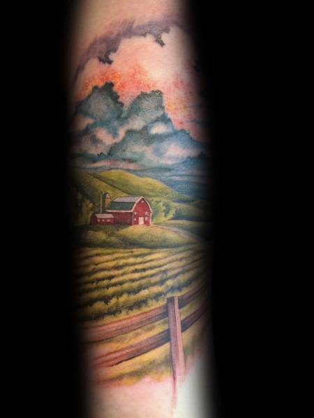 Vibrant color tattoo of a red barn on rolling green hills beneath dramatic skies, with a fence in the foreground.
