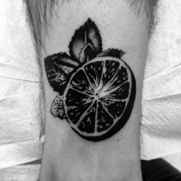 Black ink lime slice tattoo with bold shading and detailed leaves, creating a striking and stylish citrus-inspired design.