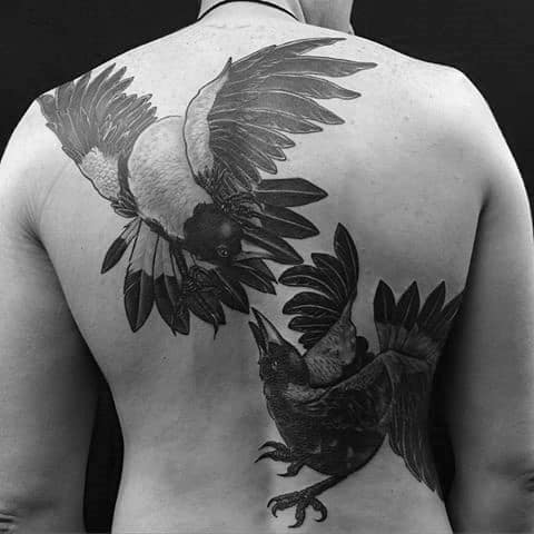 Black and gray back tattoo featuring two magpies in mid-air, wings spread wide, creating a dramatic and dynamic composition with bold shading.
