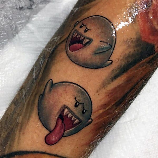 Mario ghost tattoo featuring two Boos with expressive faces, one grinning and one sticking out its tongue, shaded in black and grey on the forearm.