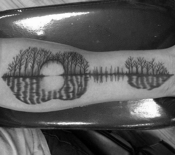 Tattoo of a landscape with trees and a sun reflected in water, creating a symmetrical, nature-inspired design along the forearm.
