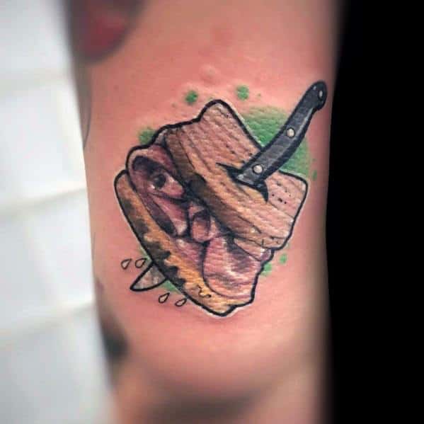 Bold sandwich tattoo with layers of meat, pierced by a knife, and a green splatter background, blending realism with a dramatic twist.