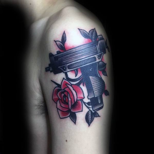 Black Uzi tattoo on the upper arm with red roses and shading. Bold contrast between the firearm and floral elements.