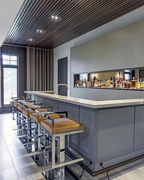 Modern home bar with grey cabinetry, chrome barstools, and a sleek metal foot rail.