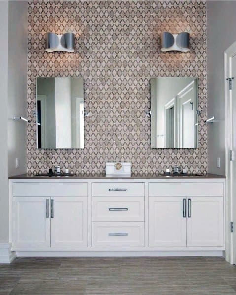 White bathroom vanity with dual mirrors, textured accent wall, and modern wall lights.