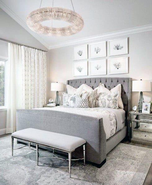 Modern bedroom with grey bed, circular crystal chandelier, and elegant decor.