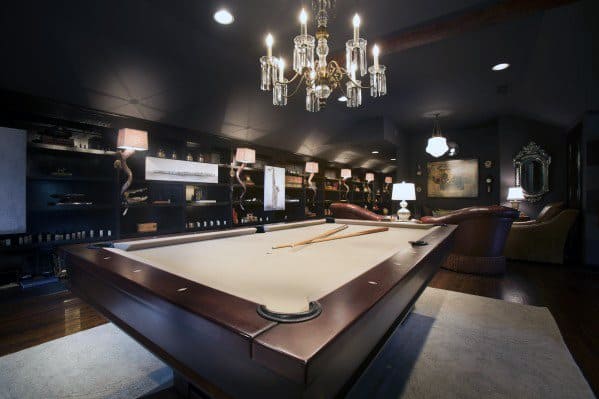 Luxurious billiard room with dark ambiance, crystal chandelier, and leather seating.