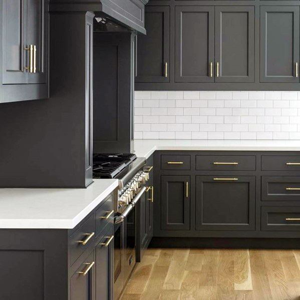 Black kitchen cabinets with gold hardware, white countertops, and a white subway tile backsplash.