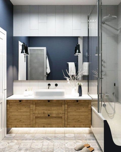 Bathroom with navy and white walls, wood vanity, patterned tile floor, and glass shower.