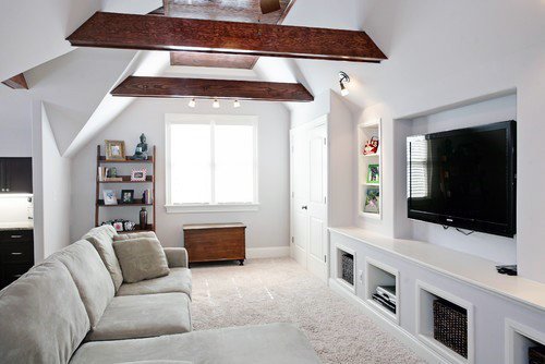 Bright living space with exposed wooden beams, sectional sofa, built-in shelves, and wall-mounted TV.