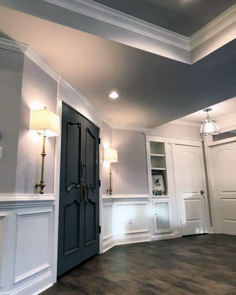 Elegant entryway featuring white chair rail molding, a dark double door, wall sconces, and hardwood flooring for a grand look