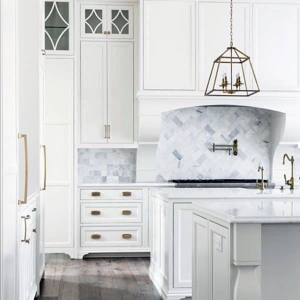 Elegant kitchen with white cabinetry, marble backsplash, gold hardware accents, and a stylish pendant light fixture