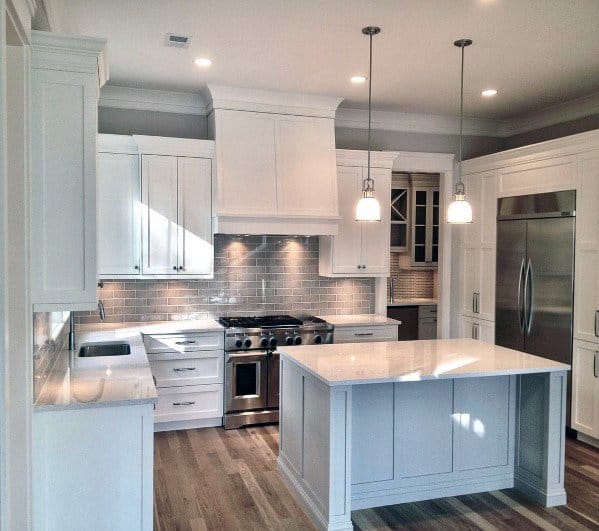 A spacious white kitchen with crown molding, pendant lighting, marble countertops, and modern appliances, offering a sleek and functional design