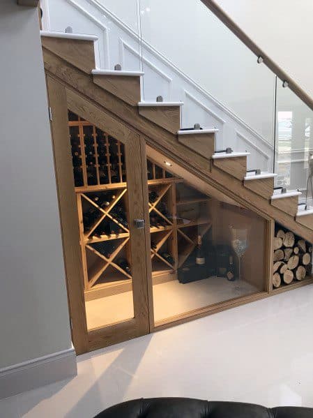 Under-the-stairs wine cellar with glass doors and firewood storage in a modern home.