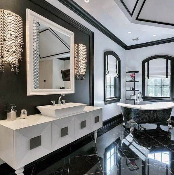 Modern bathroom with black freestanding tub, crystal lighting, and black tiled flooring.