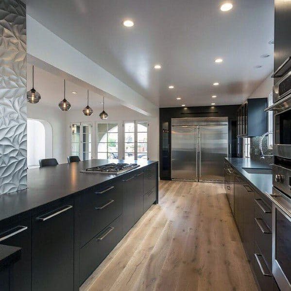Modern black kitchen with sleek cabinets, pendant lights, and light wood flooring.