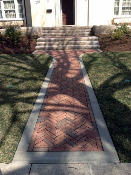 Walkway with a herringbone brick pattern leading to steps and a front door, bordered by grass
