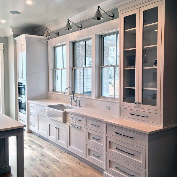 A well-lit kitchen featuring clean white cabinetry, modern fixtures, and crown molding, with natural light streaming through large windows